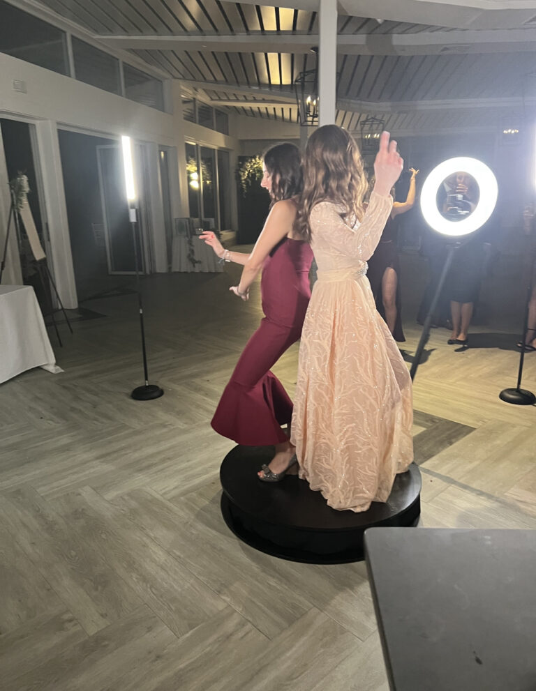 two women in dresses standing on top of the 360 photo booth platform