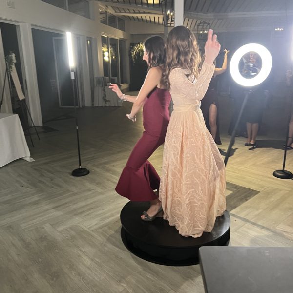 two women in dresses standing on top of the 360 photo booth platform